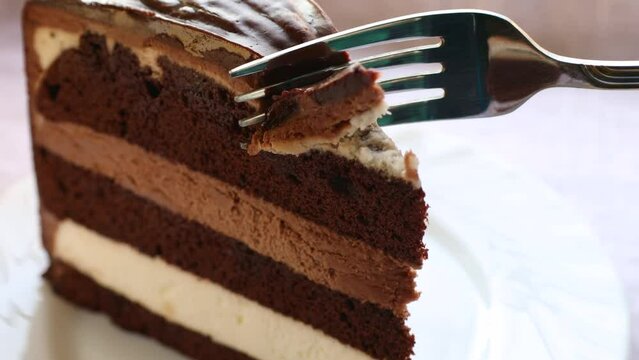 Eating triple chocolate cake piece with a fork close up