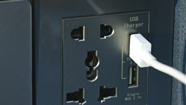 Female hand inserting white power cord cable into electric usb charger plug socket on wall close up