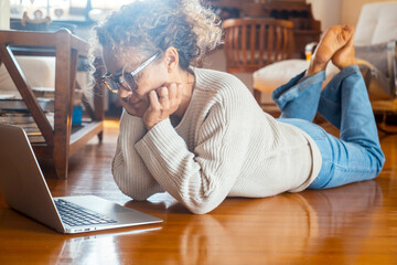 Concentrated woman using laptop at home laying barefoot on the floor. Relaxation and social media search web online leisure activity.  Relaxed female people having problems on computer connection