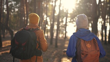 two hiker work as a team. with backpacks walking in winter in a forest park in the sunny glare at sunset. sun Two tourists travel hiking in forest park, overcoming difficulties, teamwork concept - 767008940