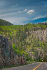 A scenic portrayal of a rough, rocky terrain covered with trees against a captivating sky with an interesting cloud formation