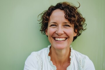 Portrait of smiling middle-aged woman with curly hair against green background - Powered by Adobe