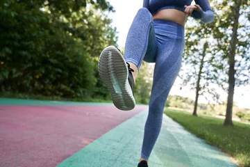 Zelfklevend Fotobehang Low angle view of unrecognizable woman jogging in the park © gpointstudio