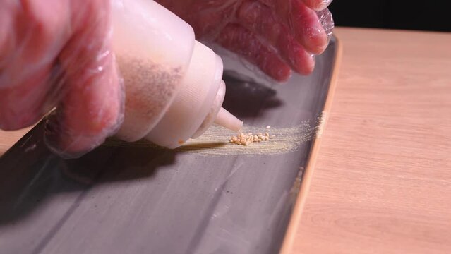 Chef decorates rectangular plate for serving sushi with sesame seeds, microgreens and wasabi. Concept of food