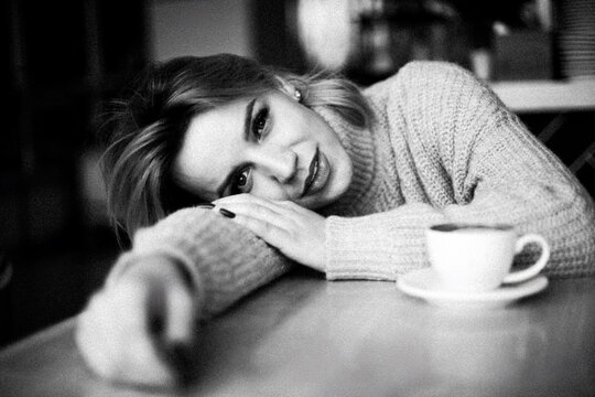 Relaxed Woman with Coffee. Woman lies on table, smiling, relaxed. Coffee cup sits in front of her. Casual, cozy scene. Enjoying a moment of relaxation. Warm ambiance