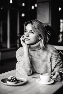 Thoughtful Woman with Coffee and Pastry. Woman sits at table, holding coffee cup with one hand, looking thoughtful. Pastry and coffee on table. Contemplative moment captured. Casual cafe scene.