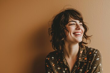 Young woman laughing and looking up on a beige wall background.