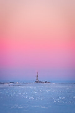 Winter evening landscape with a drilling rig in the middle of the snowy tundra in sunset lighting.