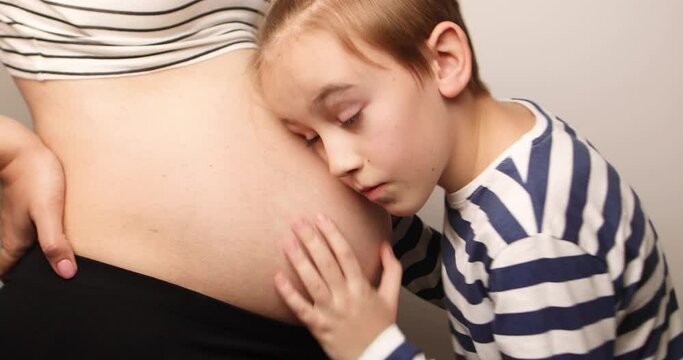 Little boy looking at her mother pregnant tummy. Pregnant mother and son spending time together at home. Pregnancy, family, parenthood, preparation and expectation concepts.