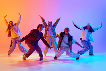 Dynamic image of young people, men and women in casual clothes dancing contemp against gradient...