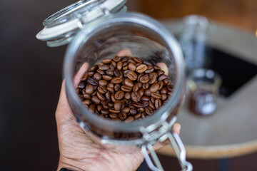 Selective focus, good quality coffee beans, shiny, dark brown in a glass jar.