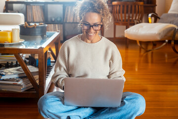 Smiling woman using laptop checking email news online sitting on the floor, searching for friends in internet social networks or working on computer, writing blog or watching webinar, studying at home