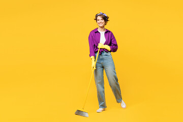 Full body young smiling happy woman she wears purple shirt casual clothes do housework tidy up hold in hand broom look camera isolated on plain yellow background studio portrait. Housekeeping concept. - obrazy, fototapety, plakaty