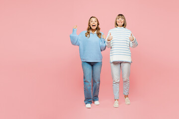 Fototapeta premium Full body happy elder parent mom with young adult daughter two women together wear blue casual clothes do winner gesture show thumb up isolated on plain pastel light pink background. Family concept.