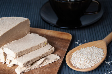 Sliced tahini halva, wooden spoon with sesame seeds and dark glass teacup close up