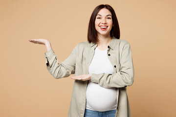 Young happy pregnant expectant woman future mom wear grey shirt with belly stomach tummy with baby point hands arms aside on area isolated on plain beige background Maternity family pregnancy concept