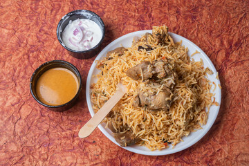 Indian mutton biryani dish served on white plate with raita and gravy.