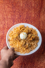 Indian chicken biryani dish served on a white plate with an egg in the middle. Closeup