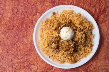 Chicken biryani is a popular Indian dish with egg in the middle. Top view of delicious chicken biryani served on white plate.