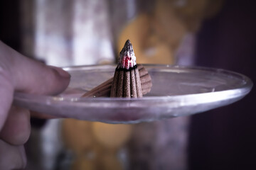 The burning embers of a burning incense are on a small plate.