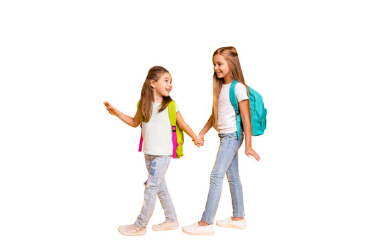 Full length body size view of two nice attractive cheerful smart clever pre-teen girls with colorful backpacks holding hands back to school isolated over bright vivid shine yellow background