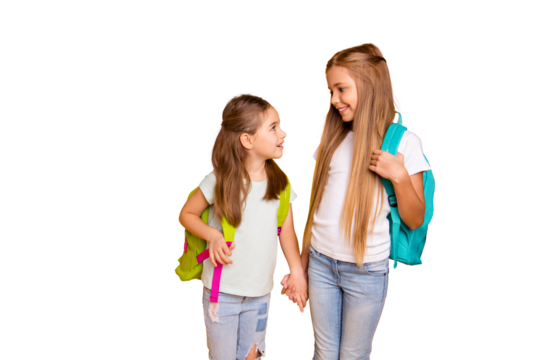 Portrait of two nice attractive lovely cheerful cheery pre-teen girls with colorful backpacks holding hands gossiping talking isolated over bright vivid shine yellow background
