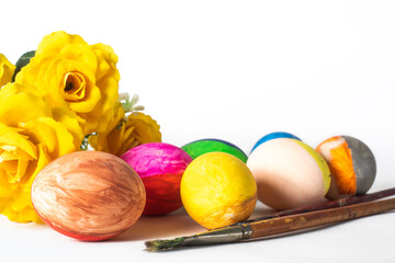 Colorful easter eggs with paint brushes and yellow flowers on a white background