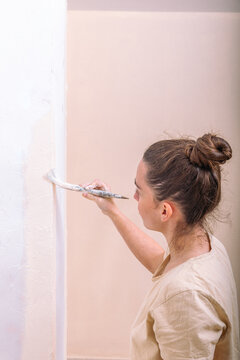 Side view of a woman carefully applying paint to a wall edge, capturing the precision required in a residential painting project