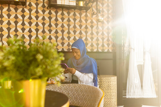Woman in blue hijab using smartphone at cafe