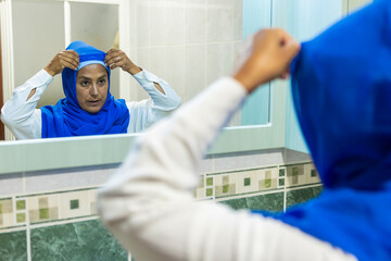Woman adjusting blue headscarf in mirror reflection