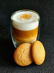 A glass of delicious latte and cookies on a black background. Delicious latte macchiato and cookies. Close-up