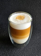 Glass mug with cappuccino isolated closeup on a black background. A cup of coffee. Hot coffee with milk in glass on black table