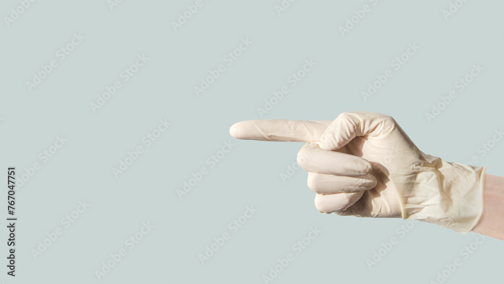 Wall mural female hand in latex glove, pointing her index finger to side at an empty space on blue background - Wall murals