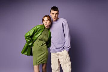 well dressed couple in vibrant clothes posing together on purple background and looking at camera
