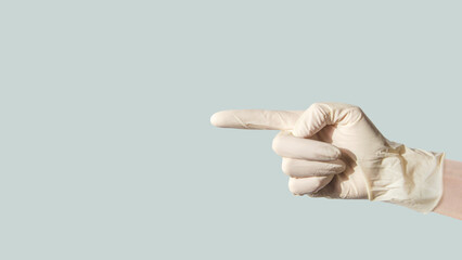 female hand in latex glove, pointing her index finger to side at an empty space on blue background