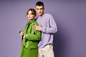 sophisticated couple in vibrant clothes posing together on purple background and looking at camera