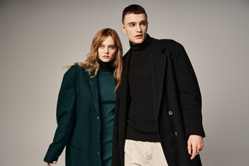 appealing man in coat posing lovingly next to his beautiful girlfriend who looking at camera