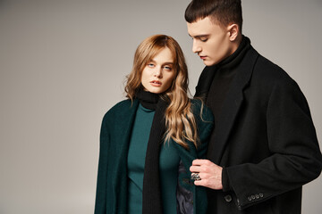 attractive man in coat posing lovingly next to his beautiful girlfriend who looking at camera