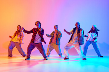 Group of five dancers in casual clothes performing with synchronized poses against gradient studio background in neon light. Concept of modern dance style, hobby, active lifestyle, youth culture