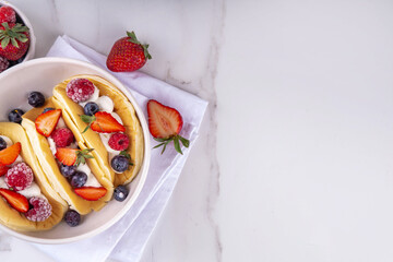 Pancake tacos. Portion of sweet dessert taco made with pancake, whipped cream, cottage cheese or ice cream, fruit and berries. Summer breakfast or brunch recipe, copy space