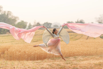 Happy young woman jumping over summer yellow field with golden wheat. Woman wearing Chinese dress jumping for joy and having fun outdoor. Freedom Concept.