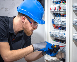 A male electrician works in a switchboard with an electrical connecting cable.
