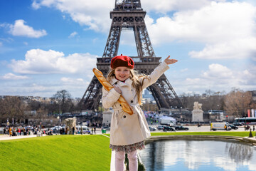 Paris travel concept with a cute blonde girl holding a french baguette bread in front of the Eiffel Tower