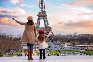 A happy mother and daughter on vacation stand in the front of the famous Eiffel Tower in Paris, France