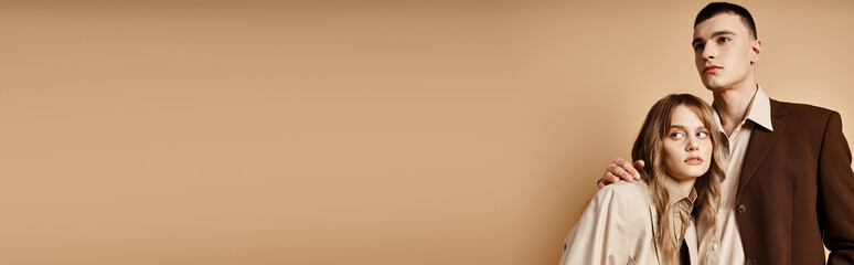 passionate debonair couple in elegant suits posing and looking at camera on pastel backdrop, banner