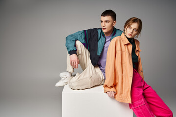 alluring woman in fashionable bomber looking at camera next to her handsome boyfriend on white cube