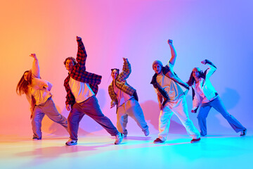 Synchronized movements. Group of young people dancing contemp against gradient studio background in neon light. Concept of modern dance style, hobby, active lifestyle, youth culture