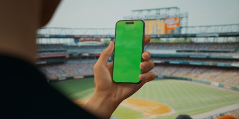 A hand holds a smartphone with a green screen at a baseball stadium - 767053367