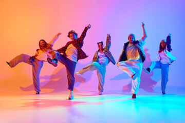 Dynamic performance of five talented dancers in motion, dancing modern dance against gradient...