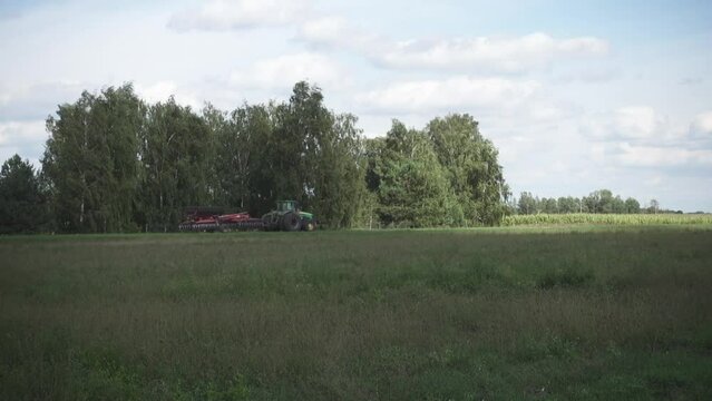Green tractor drags a large red plow. View on the field.